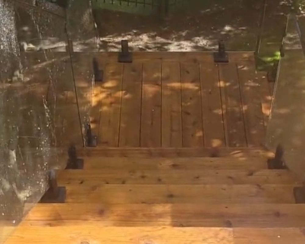 Custom deck stairs fitted with modern luxury glass railings looking down into an Oakville backyard oasis.