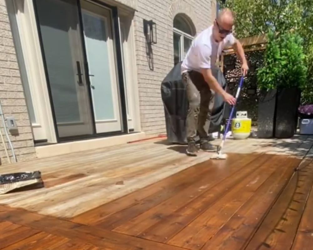 Professional deck builder applying a premium protective wood stain during a backyard deck repair in Oakville.