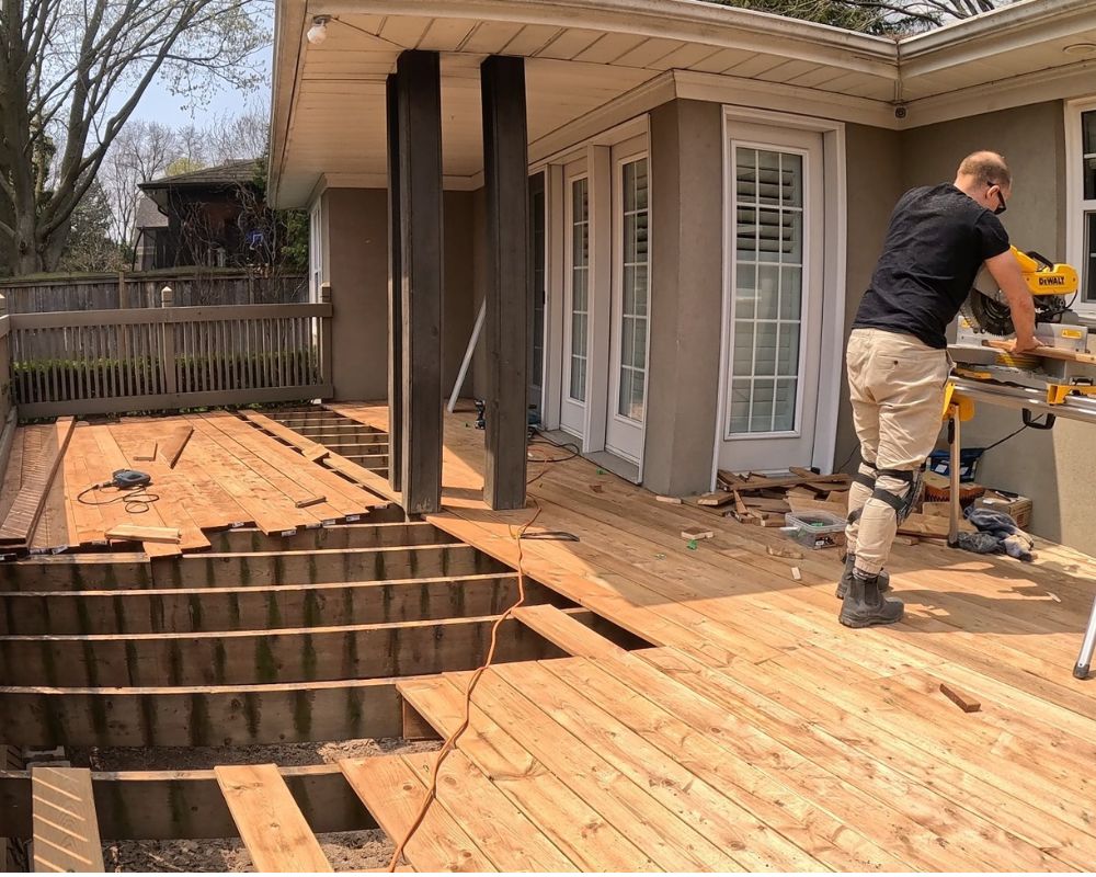 Expert deck company builder cutting brand new wood planks with a miter saw for a deck resurfacing project in Oakville.