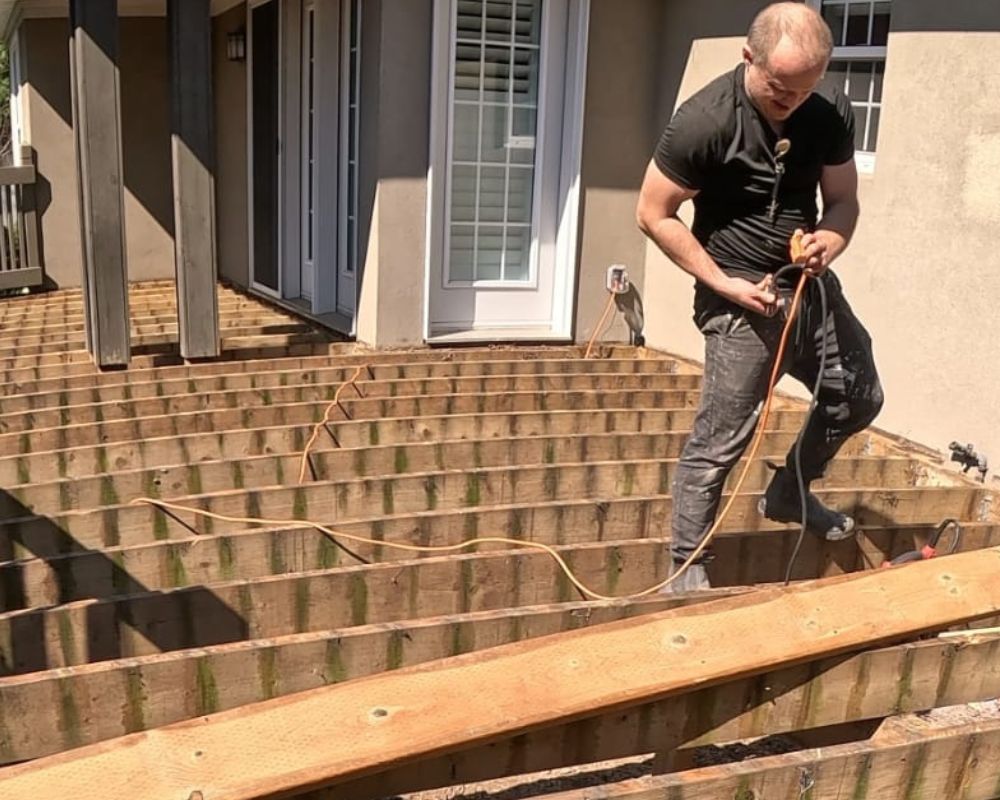 Custom deck builder using a reciprocating saw to cut and replace damaged structural joists in Oakville.