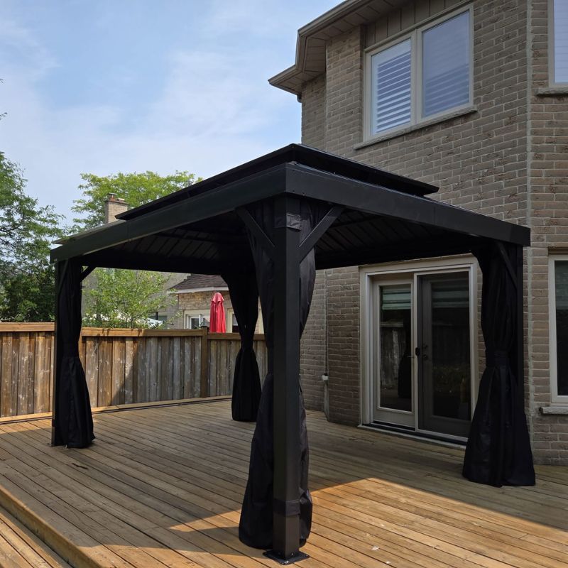 Modern black hardtop gazebo with privacy curtains installed on a wooden backyard deck in Oakville by Phil