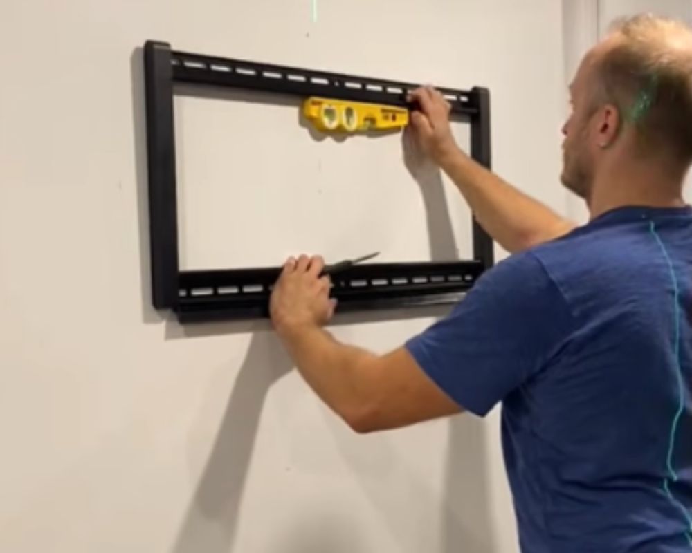 Phil using a professional spirit level tool to align a heavy-duty black steel TV wall mount bracket in Oakville